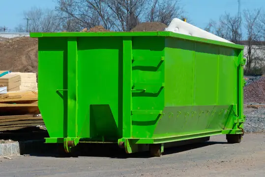 Roll-off dumpster on a construction site with dirt piles